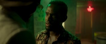 Movie still from “Yardie” (2018), directed by Idris Elba – A person wearing a floral shirt; Close Up shot, Over the shoulder angle