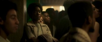 Movie still from “Yardie” (2018), directed by Idris Elba – A group of people sitting in a room; Medium shot, Over the shoulder angle