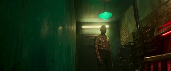 Movie still from “Yardie” (2018), directed by Idris Elba – A man standing under a green light in a room; Medium shot, Low angle
