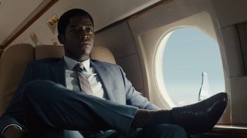 Movie still from “Snowfall” (2017), directed by Hiro Murai – A man in a suit and tie sitting on a plane; Medium shot, Low angle