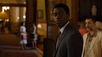 Movie still from “Snowfall” (2017), directed by Hiro Murai – A man wearing a suit and tie in a room; Medium shot, Over the shoulder angle