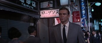 Movie still from “You Only Live Twice” (1967), directed by Lewis Gilbert – A man in a suit and tie standing in front of a building; Medium shot, Low angle