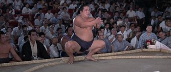 Movie still from “You Only Live Twice” (1967), directed by Lewis Gilbert – A sumo wrestler crouching down in front of a crowd; Wide shot, Low angle
