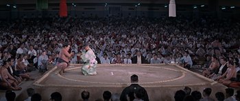 Movie still from “You Only Live Twice” (1967), directed by Lewis Gilbert – An audience watches a sumo wrestler perform a move; Extreme Wide shot, High angle
