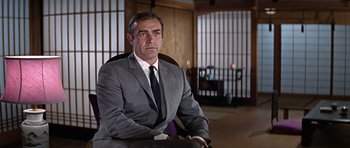 Movie still from “You Only Live Twice” (1967), directed by Lewis Gilbert – A man in a suit and tie sitting in a chair; Medium shot, Low angle