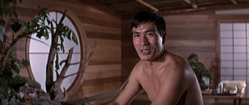 Movie still from “You Only Live Twice” (1967), directed by Lewis Gilbert – A shirtless man sitting in a wooden room; Close Up shot, Low angle