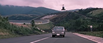 Movie still from “You Only Live Twice” (1967), directed by Lewis Gilbert – A car driving down a road with a helicopter in the background; Extreme Wide shot, Low angle