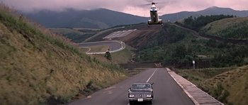 Movie still from “You Only Live Twice” (1967), directed by Lewis Gilbert – A car drives down a road while a helicopter hovers overhead; Extreme Wide shot, High angle