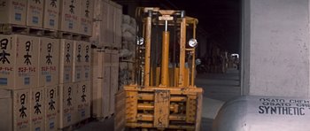 Movie still from “You Only Live Twice” (1967), directed by Lewis Gilbert – A forklift is parked in a warehouse with wooden pallets behind it; Medium shot, Low angle