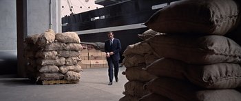 Movie still from “You Only Live Twice” (1967), directed by Lewis Gilbert – A man in a suit walking in front of a pile of bags; Wide shot, High angle