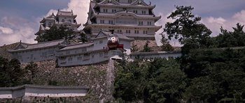 Movie still from “You Only Live Twice” (1967), directed by Lewis Gilbert – A cable car going down a hill in front of a building; Extreme Wide shot, Low angle