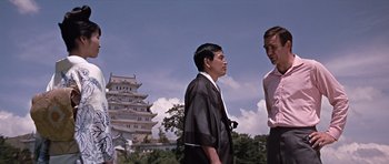 Movie still from “You Only Live Twice” (1967), directed by Lewis Gilbert – Two men standing next to each other in front of a building; Medium shot, Low angle