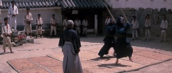 Movie still from “You Only Live Twice” (1967), directed by Lewis Gilbert – A group of men in traditional garb are practicing martial arts in an open courtyard; Wide shot, Over the shoulder angle