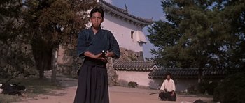 Movie still from “You Only Live Twice” (1967), directed by Lewis Gilbert – A man holding a sword while standing next to another man sitting down; Wide shot, Low angle