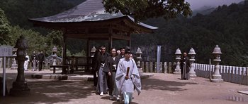 Movie still from “You Only Live Twice” (1967), directed by Lewis Gilbert – A group of people standing in front of a wooden structure; Wide shot, Low angle