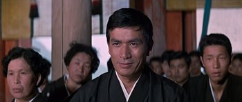 Movie still from “You Only Live Twice” (1967), directed by Lewis Gilbert – A man wearing a black robe and standing in front of other people; Close Up shot, Low angle