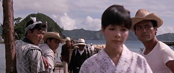 Movie still from “You Only Live Twice” (1967), directed by Lewis Gilbert – A group of people walking down a path near a body of water; Close Up shot, Over the shoulder angle