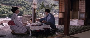 Movie still from “You Only Live Twice” (1967), directed by Lewis Gilbert – A man sitting at a table with a bird cage in the background; Wide shot, High angle