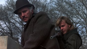 Movie still from “Young Guns” (1988), directed by Christopher Cain – A man in a top hat and a man with a gun in his hand; Close Up shot, Low angle