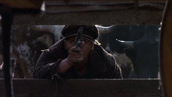 Movie still from “Young Guns” (1988), directed by Christopher Cain – A man holding a gun while standing next to a cow; Close Up shot, Low angle