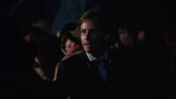 Movie still from “Young Guns” (1988), directed by Christopher Cain – A man wearing a suit and tie standing in a dark room; Close Up shot, Over the shoulder angle