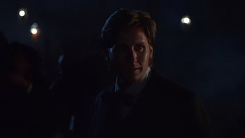 Movie still from “Young Guns” (1988), directed by Christopher Cain – A man in a suit and tie in the dark; Close Up shot, Over the shoulder angle