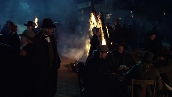 Movie still from “Young Guns” (1988), directed by Christopher Cain – A group of people sitting around a bonfire at night; Medium shot, Over the shoulder angle