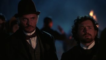 Movie still from “Young Guns” (1988), directed by Christopher Cain – A man wearing a top hat standing next to another man wearing a suit; Medium shot, Low angle