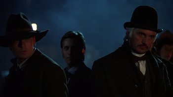 Movie still from “Young Guns” (1988), directed by Christopher Cain – A group of men standing next to each other in the dark; Close Up shot, Over the shoulder angle