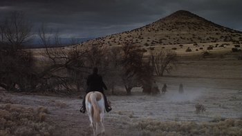 Movie still from “Young Guns” (1988), directed by Christopher Cain – A person riding a horse in a field; Extreme Wide shot, High angle