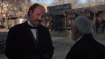 Movie still from “Young Guns” (1988), directed by Christopher Cain – A man in a suit and tie talking to another man in a suit and tie; Medium shot, Over the shoulder angle