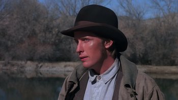 Movie still from “Young Guns” (1988), directed by Christopher Cain – A man wearing a hat standing next to a body of water; Close Up shot, Low angle