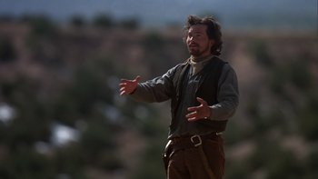 Movie still from “Young Guns” (1988), directed by Christopher Cain – A man standing on top of a hill with his arms outstretched; Medium shot, Low angle