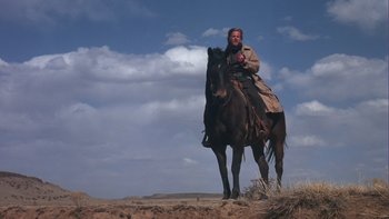 Movie still from “Young Guns” (1988), directed by Christopher Cain – A man riding a horse in the desert; Wide shot, Low angle