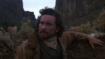 Movie still from “Young Guns” (1988), directed by Christopher Cain – A man with a beard and a cowboy hat on; Close Up shot, Low angle