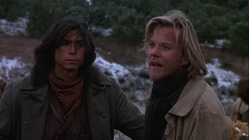 Movie still from “Young Guns” (1988), directed by Christopher Cain – Two men standing next to each other near a river; Medium shot, Over the shoulder angle