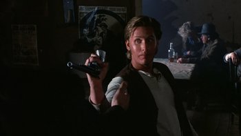 Movie still from “Young Guns” (1988), directed by Christopher Cain – A man holding a remote control in his hand; Medium shot, Over the shoulder angle