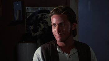 Movie still from “Young Guns” (1988), directed by Christopher Cain – A man with long brown hair wearing a white shirt and a brown vest; Close Up shot, Over the shoulder angle