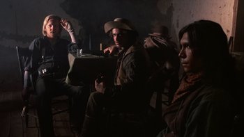 Movie still from “Young Guns” (1988), directed by Christopher Cain – A group of men sitting around a table; Medium shot, Low angle