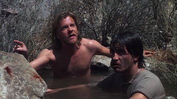 Movie still from “Young Guns” (1988), directed by Christopher Cain – Two men in a body of water with trees in the background; Medium shot, Low angle