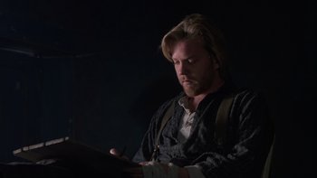 Movie still from “Young Guns” (1988), directed by Christopher Cain – A man with long hair and a beard looking down at a tablet; Medium shot, High angle