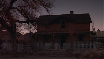 Movie still from “Young Guns” (1988), directed by Christopher Cain – An old house with a white picket fence in front of a tree; Extreme Wide shot, Low angle