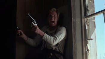Movie still from “Young Guns” (1988), directed by Christopher Cain – A man holding a toy gun in a room; Medium shot, Low angle