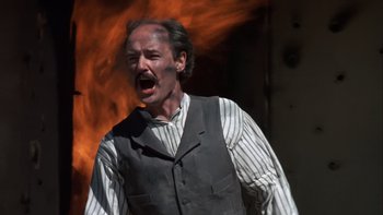 Movie still from “Young Guns” (1988), directed by Christopher Cain – A man in a vest and striped shirt is yelling in front of a fire; Close Up shot, Low angle