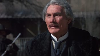 Movie still from “Young Guns” (1988), directed by Christopher Cain – An older man in a black coat and a white beard; Close Up shot, Low angle