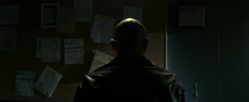 Movie still from “Zeroville” (2019), directed by James Franco – A bald headed man in a leather jacket looking at papers on a wall; Close Up shot, Over the shoulder angle
