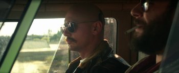 Movie still from “Zeroville” (2019), directed by James Franco – A man with a beard and sunglasses looking out of a window; Close Up shot, Over the shoulder angle