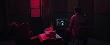 Movie still from “Zeroville” (2019), directed by James Franco – A man sitting in front of a tv with a wine bottle on it; Wide shot, High angle