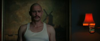 Movie still from “Zeroville” (2019), directed by James Franco – A bald man with a mustache is standing in front of a painting; Close Up shot, Low angle