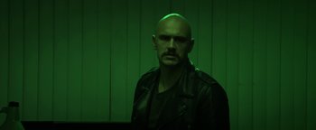 Movie still from “Zeroville” (2019), directed by James Franco – A man with a beard and a leather jacket is standing in front of a green wall; Medium shot, Low angle